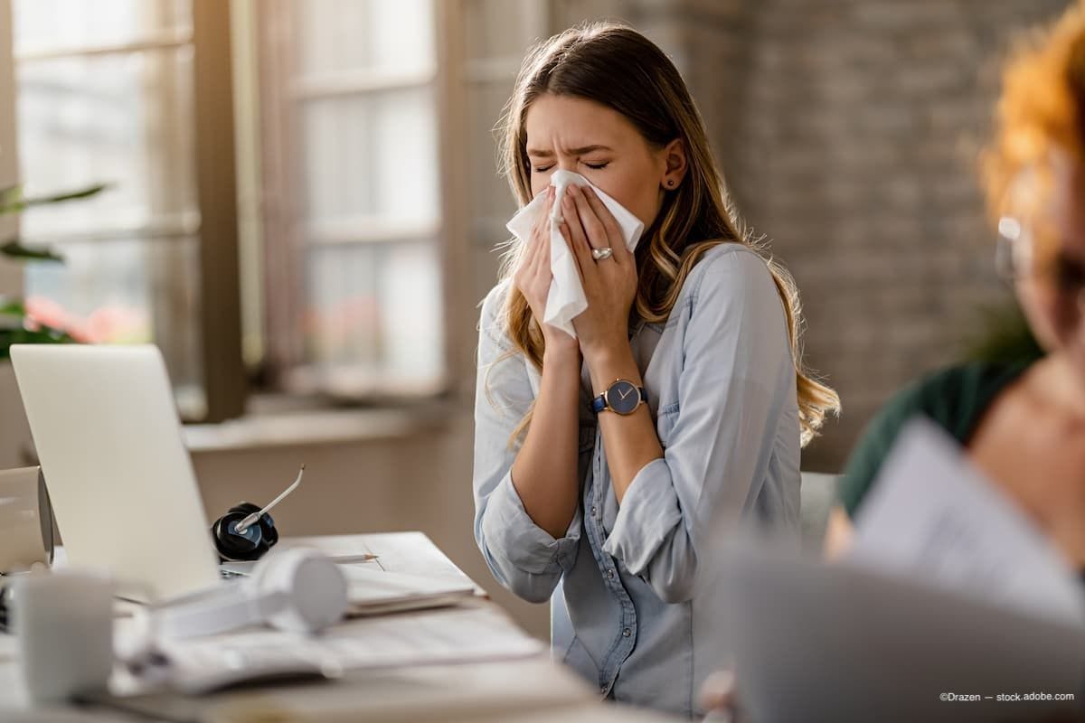 Business woman in office sneezing into tissue Image Credit: AdobeStock/Drazen