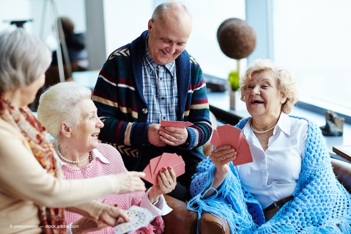 Laughing seniors sitting together playing a card game (Adobe Stock / pressmaster)