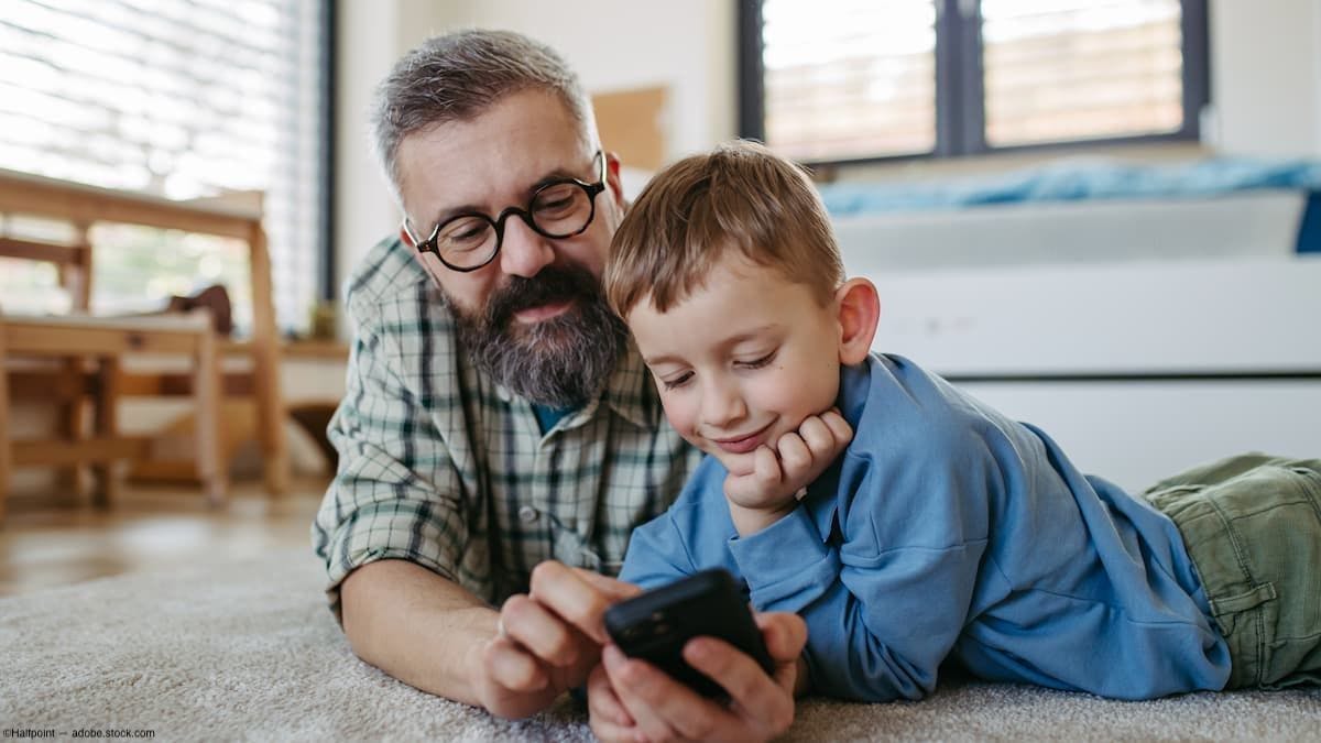 Father and son on floor looking at phone Image credit: ©Halfpoint - adobe.stock.com