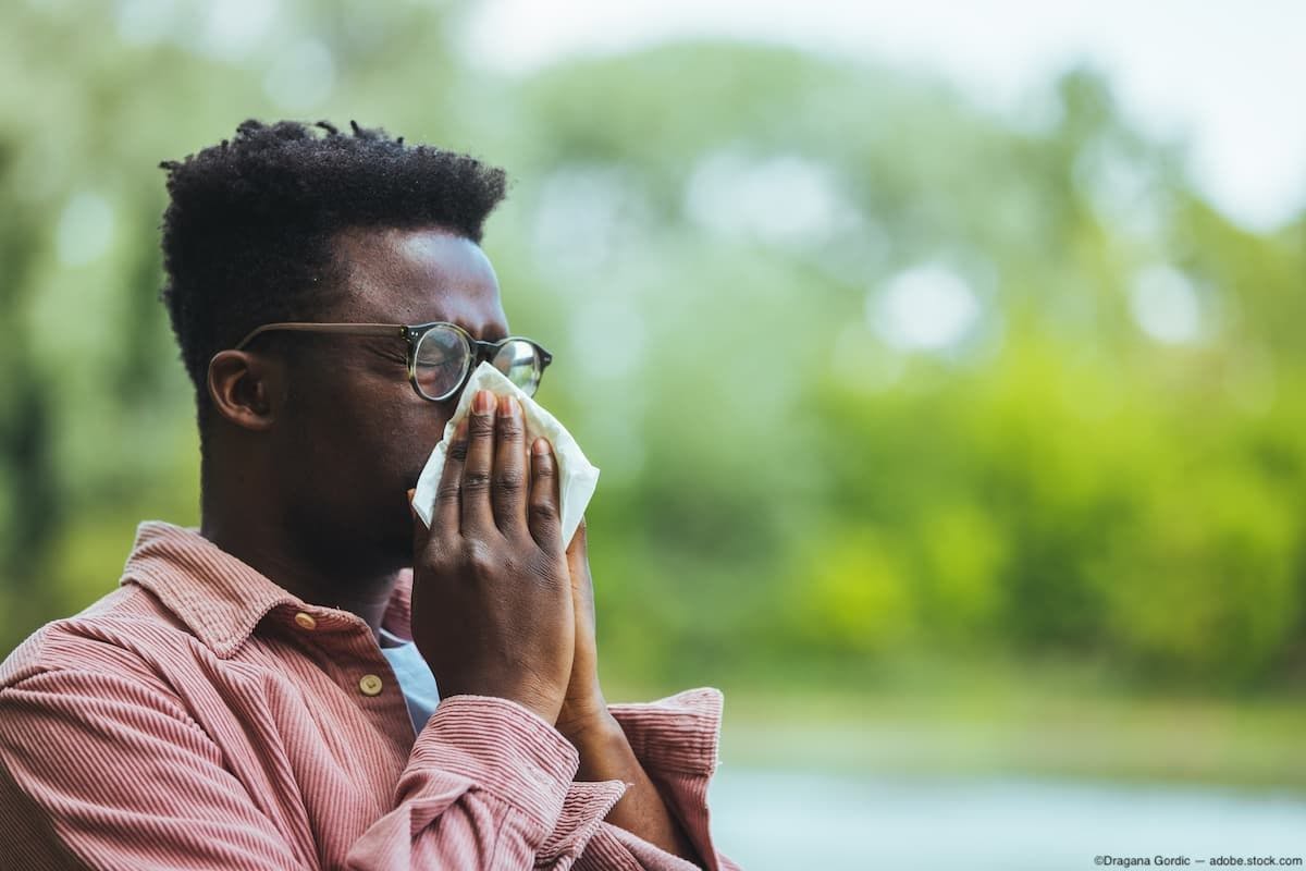 Man sitting outside sneezing into tissue Image Credit: AdobeStock/DraganaGordic
