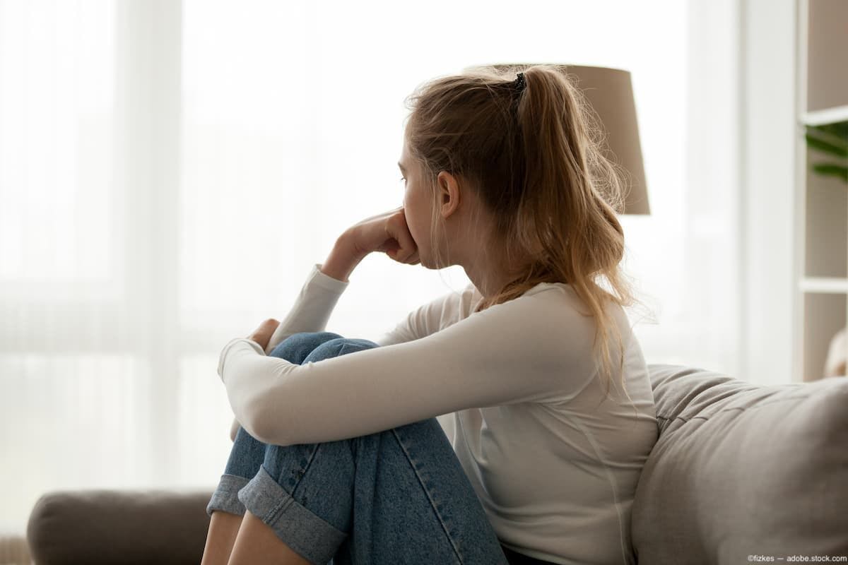 Depressed teenage girl sits on couch looking out window Image credit: ©fizkes - adobe.stock.com