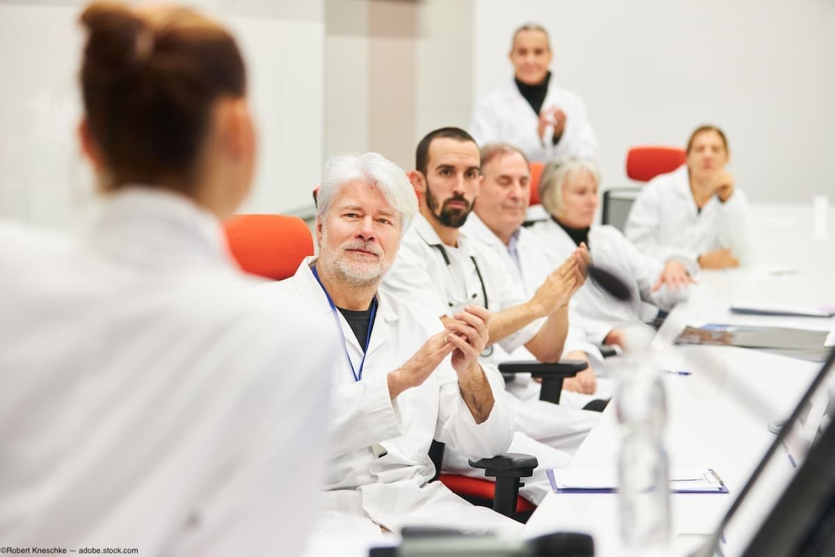 Doctors on committee table clapping Image credit: AdobeStock/RobertKneschke