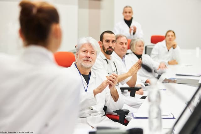 Doctors on committee table clapping Image credit: AdobeStock/RobertKneschke